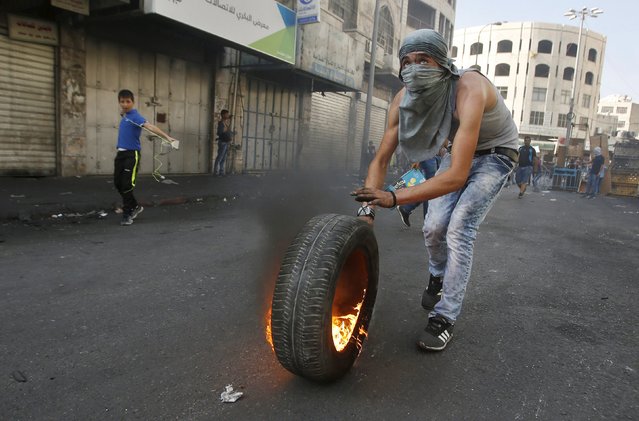 A Palestinian pushes a burning tyre during clashes with Israeli troops in the occupied West Bank city of Hebron October 4, 2015. Israeli Prime Minister Benjamin Netanyahu's office said he would meet security chiefs later on Sunday to discuss more action to tackle a rising wave of violence in East Jerusalem, which includes the Old City, and the West Bank, areas that Israel captured in a 1967 war. (Photo by Mussa Qawasma/Reuters)