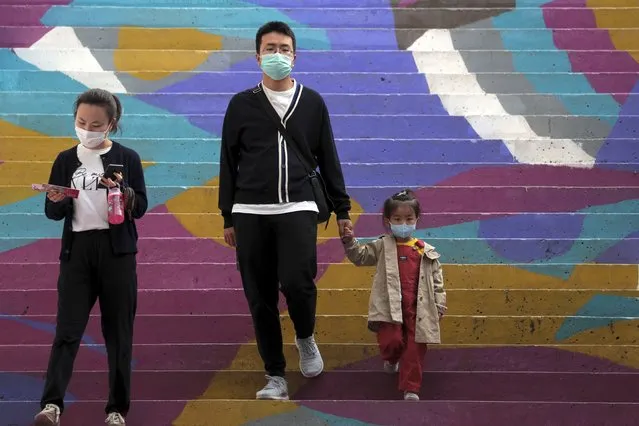 A family wearing face masks to help curb the spread of the coronavirus walk down a colourful staircase at a shopping mall in Beijing, Sunday, October 11, 2020. Even though the spread of COVID-19 has been all but eradicated in China, the pandemic is still surging across the globe with ever rising death toll. (Photo by Andy Wong/AP Photo)