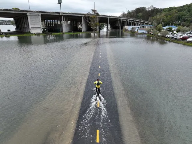 An aerial picture taken on January 3, 2022, shows a man riding his bicycle along a flooded section of the Sausalito/Mill Valley bike path during the “King Tide” in Mill Valley, California. “King Tides” occur when the Earth, moon, and sun align in orbit to produce unusually high water levels and can cause local tidal flooding. Over time, sea level rise is raising the height of tidal systems. (Photo by Josh Edelson/AFP Photo)