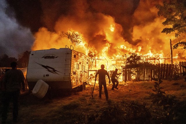 Residents work to stop flames from a burning home from spreading to a neighboring house as the 6-5 Fire burns through the Chinese Camp community of Tuolumne County, Calif., on Tuesday, September 2, 2025. (Photo by AP Photo)