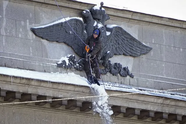 A worker clears snow from the facade of the building of the Central Bank of Russia, decorated with a bas-relief of a double-headed eagle, the coat of arms of Russia, in St. Petersburg, Russia, Thursday, March 30, 2023. (Photo by Dmitri Lovetsky/AP Photo)