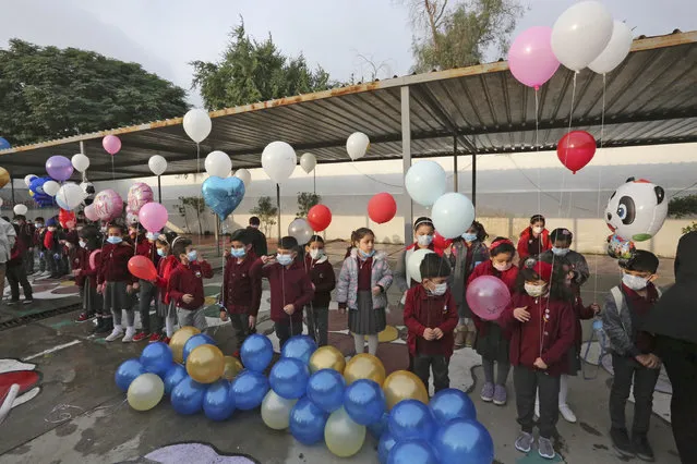 Iraqi pupils wearing protective masks hold balloons in their school yard on the first day of the new academic year, at Hariri primary school in the capital Baghdad, on November 29, 2020, amid the COVID-19 pandemic. Iraq's schools began a new academic year, after weeks of delay due to the coronavirus pandemic. Children will attend class in person once a week on rotating shifts, and will take online (distant learning) courses the rest of the week. (Photo by Sabah Arar/AFP Photo)