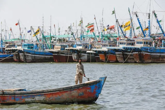 A man sails on a boat, past anchored fishing boats, after a ban was imposed on coastal activities following the cyclonic storm, Biparjoy, over the Arabian Sea, at the Ibrahim Hyderi fishing village on the outskirts of Karachi, Pakistan on June 12, 2023. (Photo by Akhtar Soomro/Reuters)