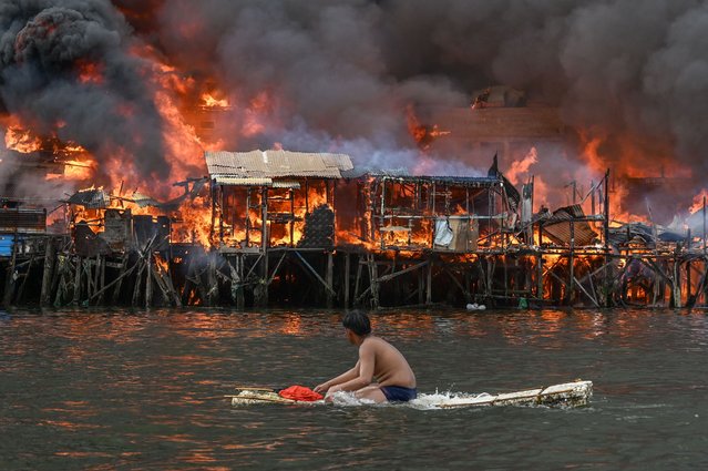 A man watches houses on fire at Tondo in Manila on November 24, 2024. Raging orange flames and thick black smoke billowed into the sky, as fire ripped through hundreds of houses in a closely built slum area of the Philippine capital Manila. (Photo by Jam Sta Rosa/AFP Photo)