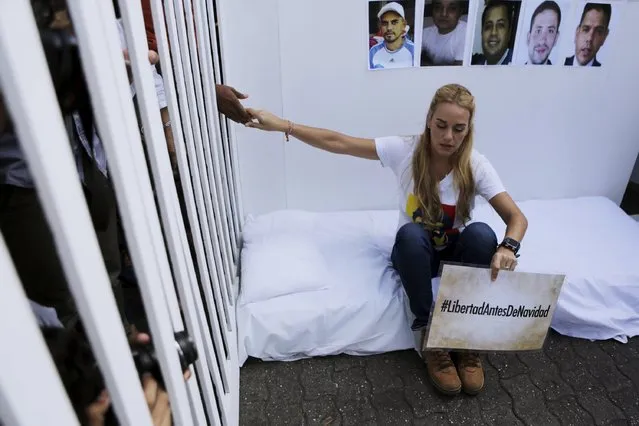 Lilian Tintori, wife of jailed Venezuelan opposition leader Leopoldo Lopez, holds the hand of a person through the bars of a mock prison cell underneath photographs of jailed opposition supporters, during a news conference in Caracas, December 14, 2015. The sign reads “Liberty before Christmas”. (Photo by Marco Bello/Reuters)