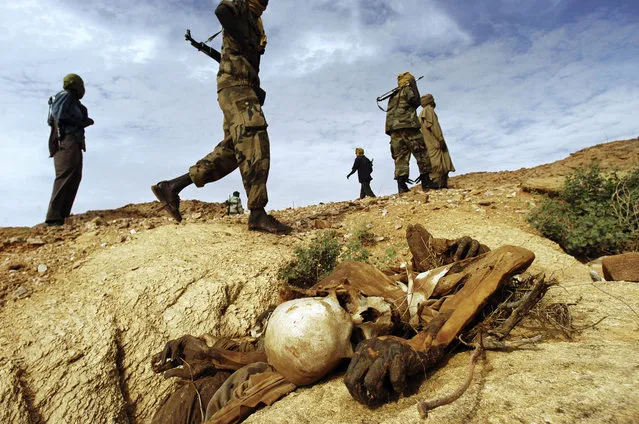 Sudanese Liberation Army soldiers walk past a dead body left from an attack on civilians in the district of Farawiya, Darfur, August 24, 2004. Sixteen bodies lay in the surrounding ravines after men from five nearby villages were allegedly killed by Janjaweed militias backed by Sudanese government forces. (Photo by Lynsey Addario)