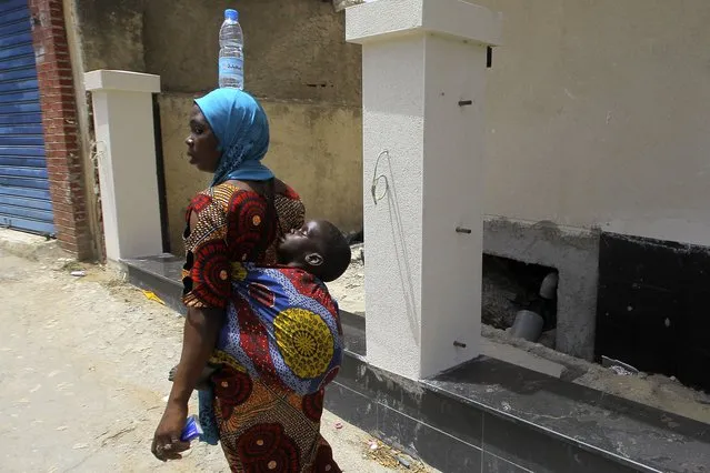 A woman from Niger carries her baby and a bottle of water on her head, Saturday, July 8, 2023. (Photo by Anis Belghoul/AP Photo)