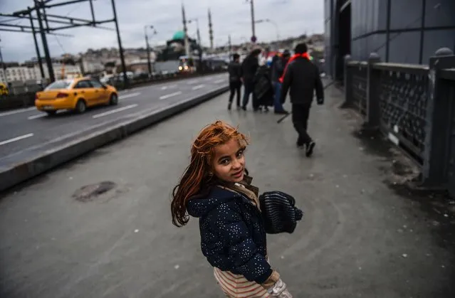 A Syrian refugee girl begs on the Galata Bridge on a rainy day in Istanbul on November 30, 2016. (Photo by Bulent Kilic/AFP Photo)