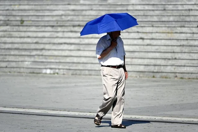 A man walks with an umbrella to shield from the sun in Pristina on July 17, 2023, as Kosovo is hit by a heatwave. (Photo by Armend Nimani/AFP Photo)