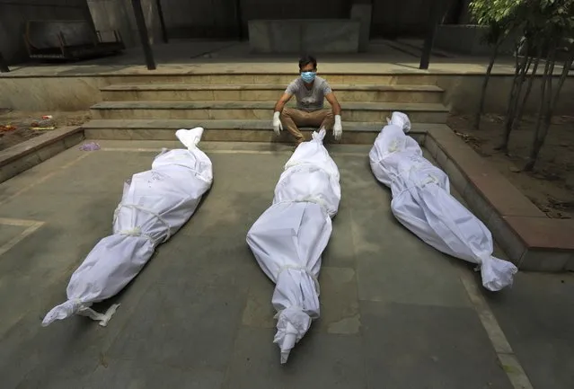 A man waits for the cremation of a relative who died of COVID-19, placed near bodies of other victims, in New Delhi, India, Tuesday, April 20, 2021. India has been overwhelmed by hundreds of thousands of new coronavirus cases daily, bringing pain, fear and agony to many lives as lockdowns have been placed in Delhi and other cities around the country. (Photo by AP Photo/Stringer)