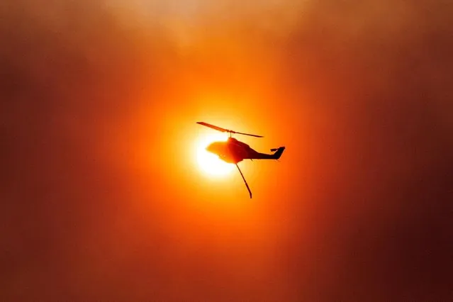 A firefighting helicopter is silhouetted in front of the sun, as a wildfire burns in Mandra, Greece on July 18, 2023. (Photo by Alkis Konstantinidis/Reuters)