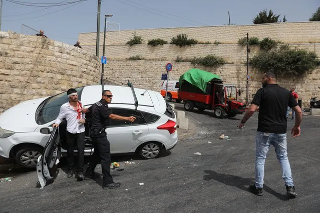 An Israeli policeman (c) points a gun at a Palestinian man (r) next to a wounded Orthodox Jewish man (l) that crashed his car near the Lions' Gate, as clashes continue at the Temple Mount in the old city of Jerusalem, 10 May 2021. Protests continue in support of six Palestinian families facing eviction in the neighborhood of Sheikh Jarrah in favor of Jewish families who claimed they used to live in the houses before fleeing in the 1948 war that led to the creation of Israel. Thousands of Israelis, including right-wing groups, were expected to join the “Flag March” on 10 May which is considered “Jerusalem Day”, an Israeli national holiday that celebrates the establishment of Israeli control over the Old City in the aftermath of the June 1967 Six-Day War. (Photo by Abir Sultan/EPA/EFE)