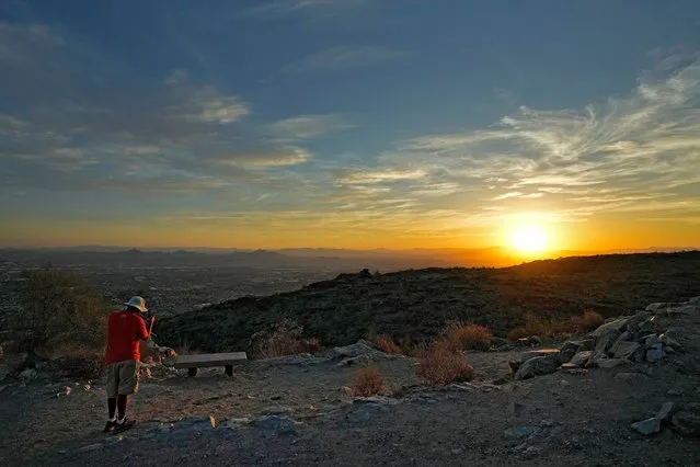 A hiker photographs the sun rising over the Valley atop South Mountain, Monday, July 17, 2023 Phoenix. Phoenix is set to break its own record for consecutive days of highs of at least 110 degrees. Around one-third of Americans are under some type of heat advisory, with the most blistering temperatures in the South and West, where even the regular simmer has turned up a notch. (Photo by Matt York/AP Photo)