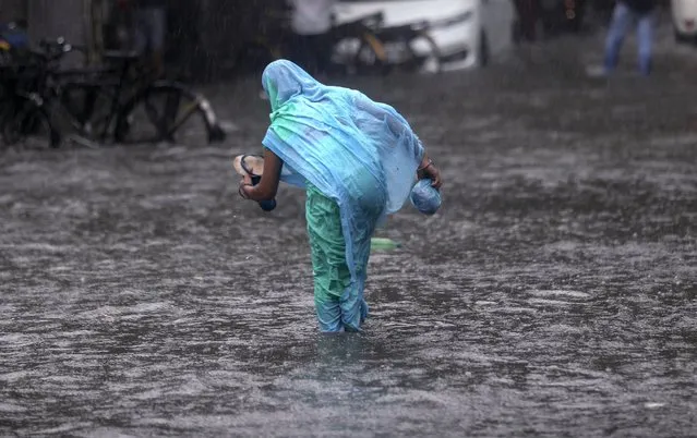 A woman tries to make her way through a flooded street during heavy rains in Mumbai, India, Wednesday, June 9, 2021. (Photo by Rafiq Maqbool/AP Photo)