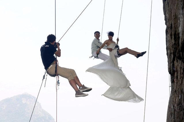 A photographer takes pictures of Fang in a wedding gown next to her husband as they hang from a cliff during a rock climbing exercise in Liuzhou, on Oktober 27, 2013. (Photo by Reuters/Stringer)