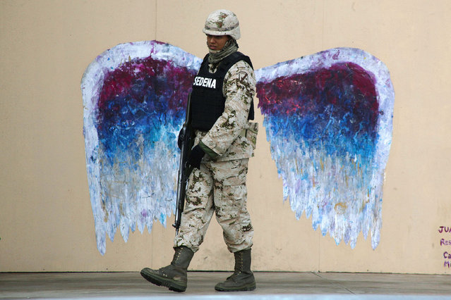 A soldier walks past graffiti depicting angel wings by artist Colette Miller in Ciudad Juarez, Mexico March 18, 2015. (Photo by Jose Luis Gonzalez/Reuters)