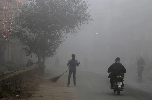 A sweeper cleans a street in heavy fog, in Lahore, Pakistan, Monday, December12, 2016. Various cities in eastern and central Pakistan continue to experience heavy fog, disrupting air and road transportation. (Photo by K.M. Chaudary/AP Photo)