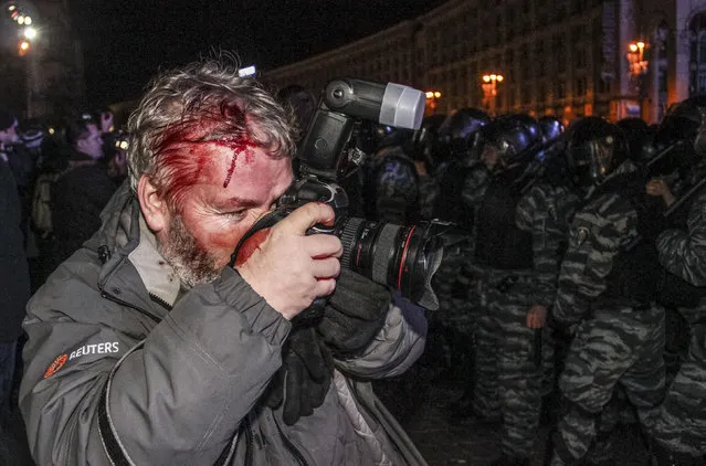 Wounded Reuters photographer Gleb Garanich, who was injured by riot police, takes pictures as riot police block protesters during a scuffle at a demonstration in support of EU integration at Independence Square in Kiev November 30, 2013. Riot police in the Ukrainian capital Kiev used batons and stun grenades to disperse hundreds of pro-Europe protesters from the city's main Independence Square early on Saturday, witnesses said. (Photo by Reuters/Stringer)