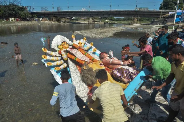 Hindu devotees immerse an idol of the ten-handed Hindu Goddess Durga in the Mahananda River during the final day of Durga Puja festival in Siliguri on October 15, 2021. (Photo by Diptendu Dutta/AFP Photo)
