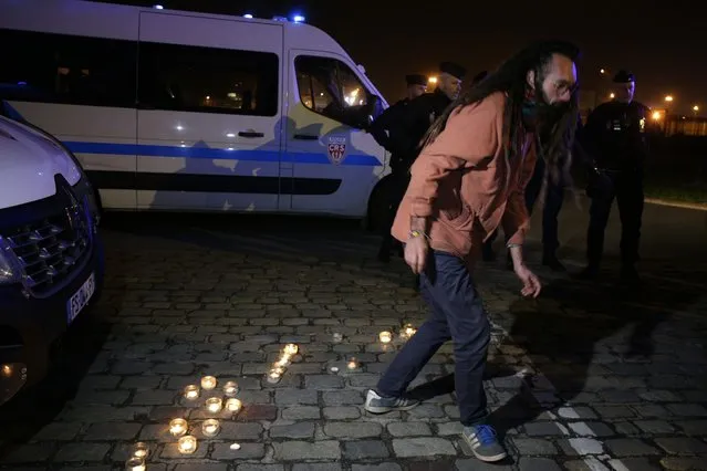 An activist leaves after lighting up a candle outside the port of Calais, northern France, Wednesday, November 24, 2021. At least 31 migrants bound for Britain died Wednesday when their boat sank in the English Channel, in what France's interior minister called the biggest tragedy involving migrants on the dangerous crossing to date. (Photo by Michel Spingler/AP Photo)