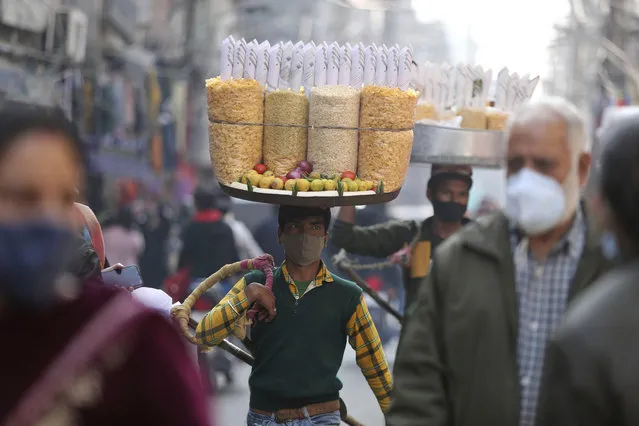 A snacks vendor wears a face mask as a precaution against COVID-19 and walks in a market area in Jammu, India, Saturday, November 27, 2021. (Photo by Channi Anand/AP Photo)
