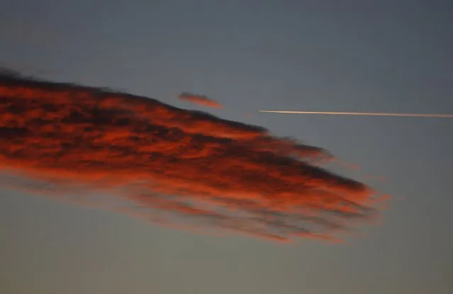 An airplane leaves a vapor trail as it flies past a cloud during dusk as seen from Paracuellos del Jarama, Spain, March 3, 2016. (Photo by Sergio Perez/Reuters)