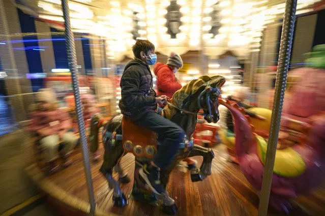 Children, some wearing face masks, enjoy a carousel ride at a Christmas fair in Bucharest, Romania, Saturday, November 27, 2021. The Romanian capital will have three Christmas fairs open for public in the coming weeks and access to the venues will be conditioned by a COVID-19 green pas, proving the holder's vaccination or recovery after the infection. (Photo by Vadim Ghirda/AP Photo)