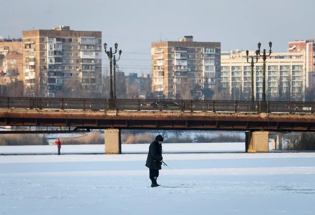 A man fishes on the ice-covered Kalmius river in the rebel-held city of Donetsk, Ukraine on January 26, 2022. (Photo by Alexander Ermochenko/Reuters)