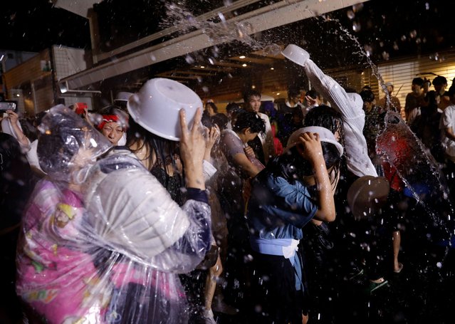 Spectators cover themselves with plastic basins while others throw hot spring water to revellers carrying a portable shrine, a Mikoshi, during a parade at the Yukake Matsuri, the hot spring water splashing festival, in Yugawara, Kanagawa Prefecture, Japan, on May 25, 2024. About 60 tons of hot spring water was used for this festival which started 41 years ago to promote the hot spring village, an organizer said. (Photo by Kim Kyung-Hoon/Reuters)