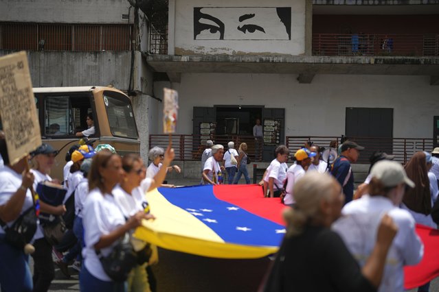 People demand higher pensions, marking National Senior Day, in front of a mural depicting the eyes of late President Hugo Chavez in Caracas, Venezuela, May 29, 2024. (Photo by Ariana Cubillos/AP Photo)