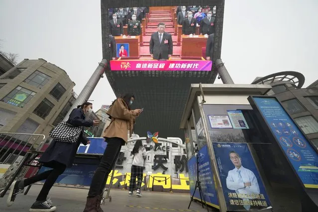 Women scan health check QR codes to enter a shopping mall as a large video screen shows Chinese President Xi Jinping during coverage of the closing session of China's National People's Congress (NPC) in Beijing, Friday, March 11, 2022. (Photo by Ng Han Guan/AP Photo)