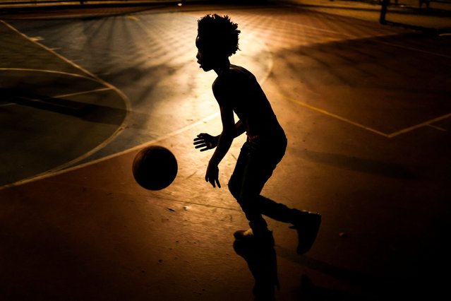 A young boy plays basketball at night on a playground of Harlem in New York City on August 14, 2024. (Photo by Charly Triballeau/AFP Photo)