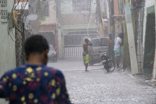 A man stands under a roof drain as the rain of Tropical Storm Franklin fall on Santo Domingo, Dominican Republic, Tuesday, August 22, 2023. (Photo by Ricardo Hernandez/AP Photo)