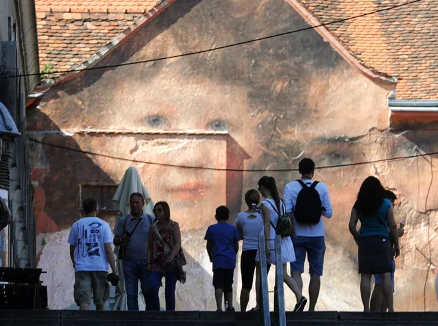 Tourists walk near an artwork of artist Julien De Casablanca on a facade in downtown Zagreb, 11 June 2017. Julien De Casablanca is French and Corsican visual artist and filmmaker who launched Outings Project, which consists in bringing paintings from museum walls into the streets all over the world and In Zagreb he will present his exhibition from 06-28 June this year. (Photo by  Antonio Bat/EPA)
