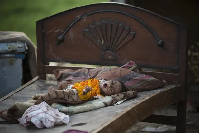 A child of a Pakistani nomad family sleeps outside her makeshift home as she gets swamped with flies in Islamabad, Pakistan, Wednesday, August 5, 2015. Some Pakistanis, mostly nomad families, live in unhygienic conditions in suburbs and earn their living by selling balloons and toys. (Photo by B. K. Bangash/AP Photo)