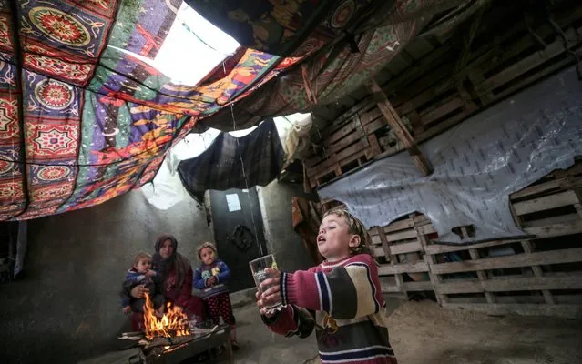 A child fills a glass with rainwater dripping from the covered ceiling in front of a woman and two children warming around a fire in a makeshift house on a cold day during winter in al-Amal neighborhood of Beit Lahia district in Gaza City, Gaza on January 22, 2020. (Photo by Mustafa Hassona/Anadolu Agency via Getty Images)
