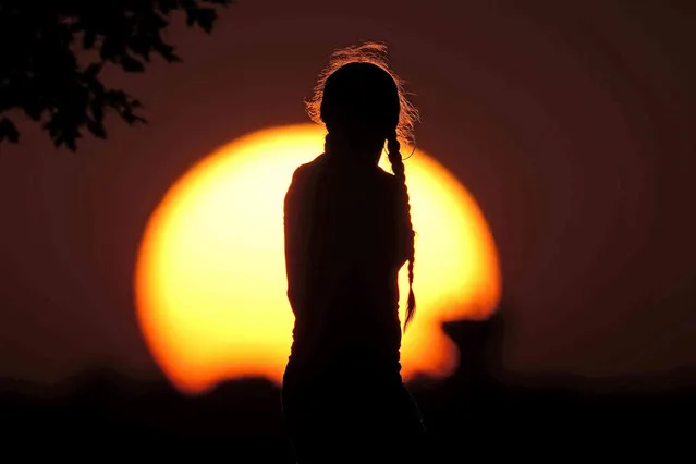 A girl watches the sunset as she waits to watch fireworks from a park Monday, July 4, 2022, in Kansas City, Mo. (Photo by Charlie Riedel/AP Photo)