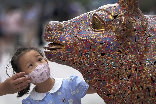 A child wearing a face mask takes a closer look at a bull sculpture titled “Five Bulls Gathering Fortune” at the Wangfujing shopping district in Beijing, Tuesday, August 9, 2022. (Photo by Andy Wong/AP Photo)