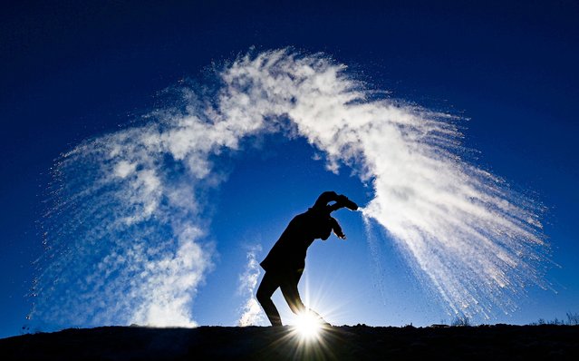 A woman throws hot water from a thermos bottle into the cold air making its three phases visible – liquid, gas, solid – as the smallest droplets cool and evaporate in a dramatic cloud before they reach the ground as snow, in Berlin on a sunny but frosty Boxing Day, on December 26, 2021. (Photo by Tobias Schwarz/AFP Photo)