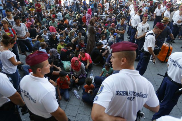 Hungarian police officers watch migrants outside the main Eastern Railway station in Budapest, Hungary, September 1, 2015. (Photo by Laszlo Balogh/Reuters)