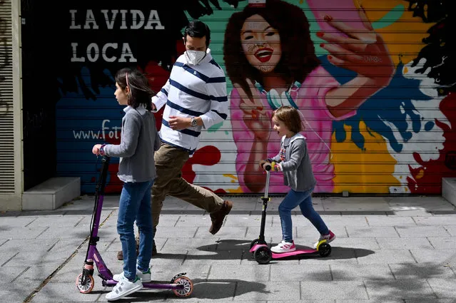 Children skate on scooters accompanied by an adult in Madrid on April 26, 2020 during a national lockdown to prevent the spread of the COVID-19 disease. (Photo by Gabriel Bouys/AFP Photo)