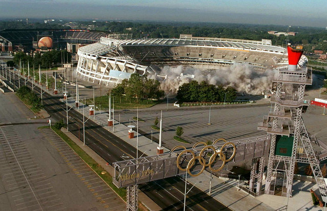 The Olympic Caldron can be seen in the foreground as explosive charges weaken the structure holding up at Fulton County Stadium Saturday, August 2, 1997, in Atlanta. The stadium, home of the Braves from1966-1996, was imploded to make room for a parking lot for the Braves new home shown in the background. (Photo by Alan Mothner/AP Photo)