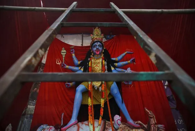 A man arranges a backdrop behind the giant idol of Goddess Kali during the “Dashain”, Hinduism's biggest religious festival, in Kathmandu September 25, 2014. Hindus in Nepal celebrate victory over evil during the festival by flying kites, feasting, playing swings, sacrificing animals and worshipping the Goddess Durga as well as other gods and goddesses, as part of celebrations held throughout the country. (Photo by Navesh Chitrakar/Reuters)