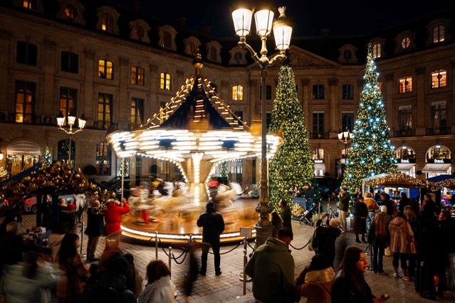 People stand around a spinning carousel at the Place Vendome ahead of Christmas celebrations in central Paris on December 8, 2023. (Photo by Dimitar Dilkoff/AFP Photo)
