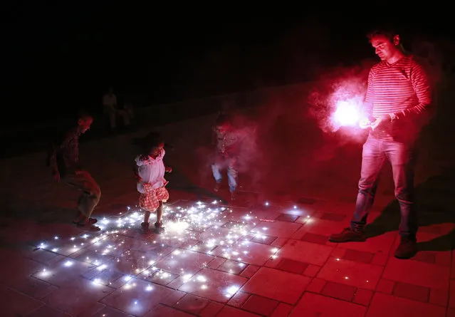 A man lights firecrackers as children dance on them while celebrating the Hindu festival of Diwali, the annual festival of lights, in Mumbai October 23, 2014. (Photo by Danish Siddiqui/Reuters)