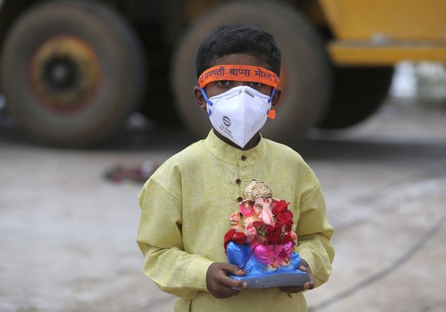 An Indian child wearing a mask as a precaution against the coronavirus carries an idol of elephant-headed Hindu god Ganesha to immerse in Saroornagar Lake on the final day of Ganesh Chaturthi festival in Hyderabad, India, Tuesday, September 1, 2020. The festival is a celebration of the birth of Ganesha, the Hindu god of wisdom, prosperity and good fortune. (Photo by Mahesh Kumar A./AP Photo)