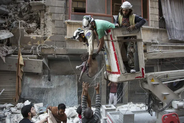 Syrian rescuers hand the body of a girl down to civilians on the ground after she was pulled from rubble of a budling following government forces air strikes in the rebel held neighbourhood of Al-Shaar in Aleppo on September 27, 2016. Syria's army took control of a rebel-held district in central Aleppo, after days of heavy air strikes that have killed dozens and sparked allegations of war crimes. (Photo by Karam Al-Masri/AFP Photo)