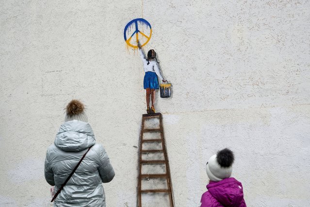 A woman and a child look at an artwork of the famous street artist Tvboy, created on a wall of a local lyceum (a school), amid Russia's attack on Ukraine, in the town of Bucha, outside Kyiv, Ukraine on January 29, 2023. (Photo by Valentyn Ogirenko/Reuters)