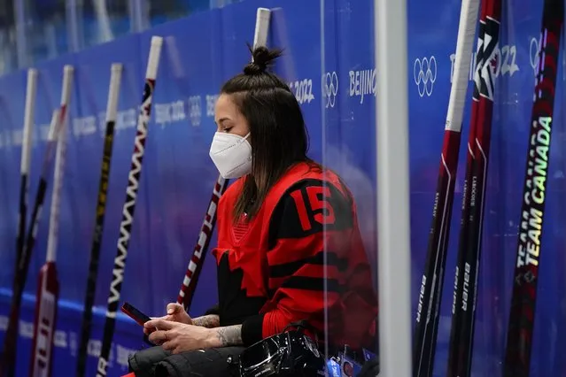 Canadian ice hockey player Melodie Daoust looks at her smart phone as players take souvenir photos at the 2022 Winter Olympics, Wednesday, February 2, 2022, in Beijing. (Photo by Matt Slocum/AP Photo)