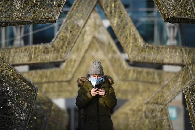 A woman wearing a face mask uses her smartphone walking through star shaped festive decorations set for the upcoming New Year and Christmas holidays outside a shopping centre in Moscow on December 11, 2020, amid the ongoing coronavirus disease pandemic. (Photo by Natalia Kolesnikova/AFP Photo)